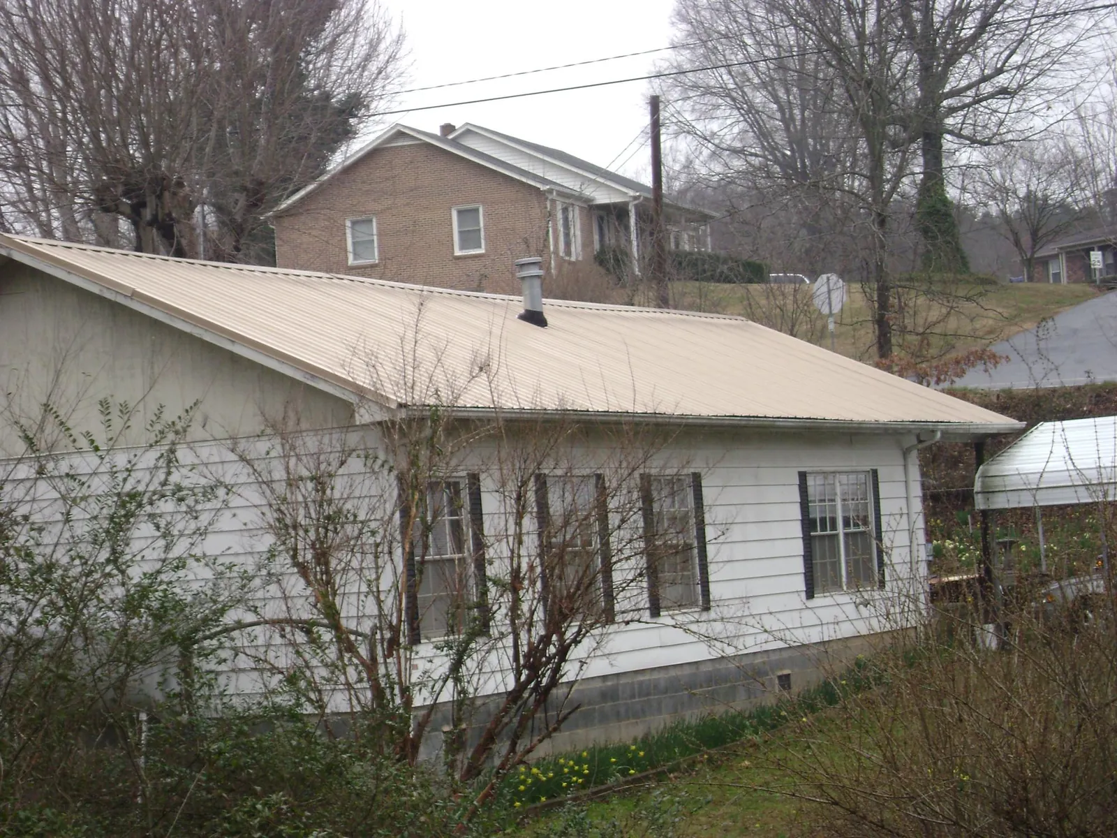 Tan metal roof on a white sided house set into a hillside — Commercial Roofing by Roofing Brothers in Charlestown